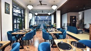 A modern dining area with blue chairs, wooden tables, and chandeliers. - LA Riqueza Koala Inn Mcleod Ganj - Near to Dalai Lama Temple & Mall Road (Dharamshala)