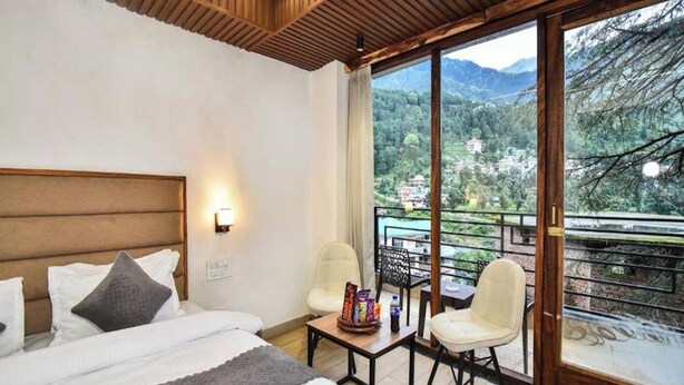 Ein Hotelzimmer mit Bett, einem kleinen Tisch mit Stühlen und einem Balkon mit Bergblick.