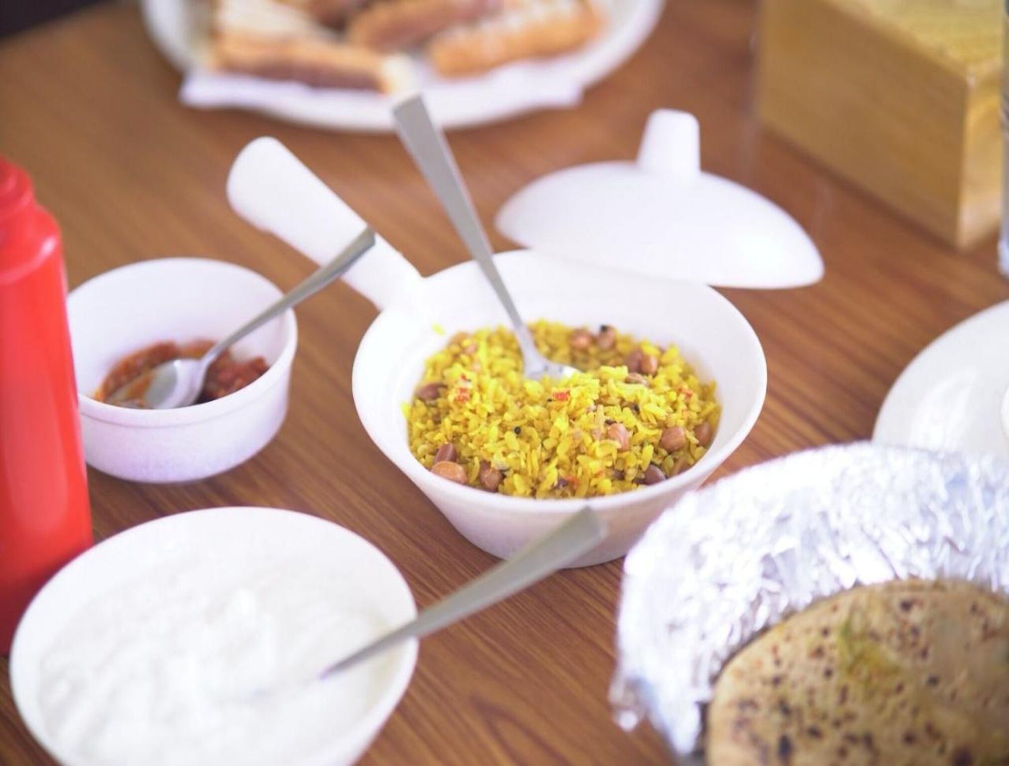 Une table sur laquelle se trouvent divers aliments, notamment un bol de riz jaune aux haricots, un bol de sauce rouge et une assiette de nourriture blanche, qui pourrait être du yaourt ou du fromage.
