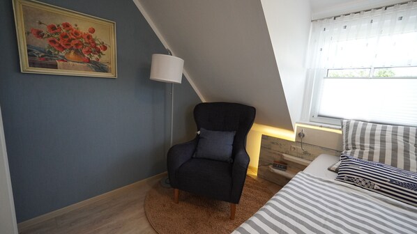 A bedroom with a bed, a chair, a lamp, a painting, and a window.