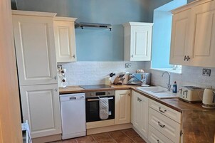 Una cocina compacta con armarios blancos, lavavajillas, estufa y pileta.