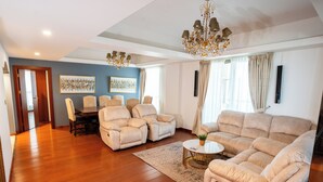 Een ruime woonkamer met een grote beige bank, twee fauteuils, een salontafel en een kroonluchter.