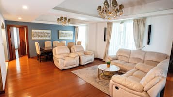 A spacious living room with a large beige sofa, two armchairs, a coffee table, and a chandelier.