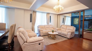 Een ruime woonkamer met een houten vloer, beige banken, een eettafel met stoelen en een kroonluchter.