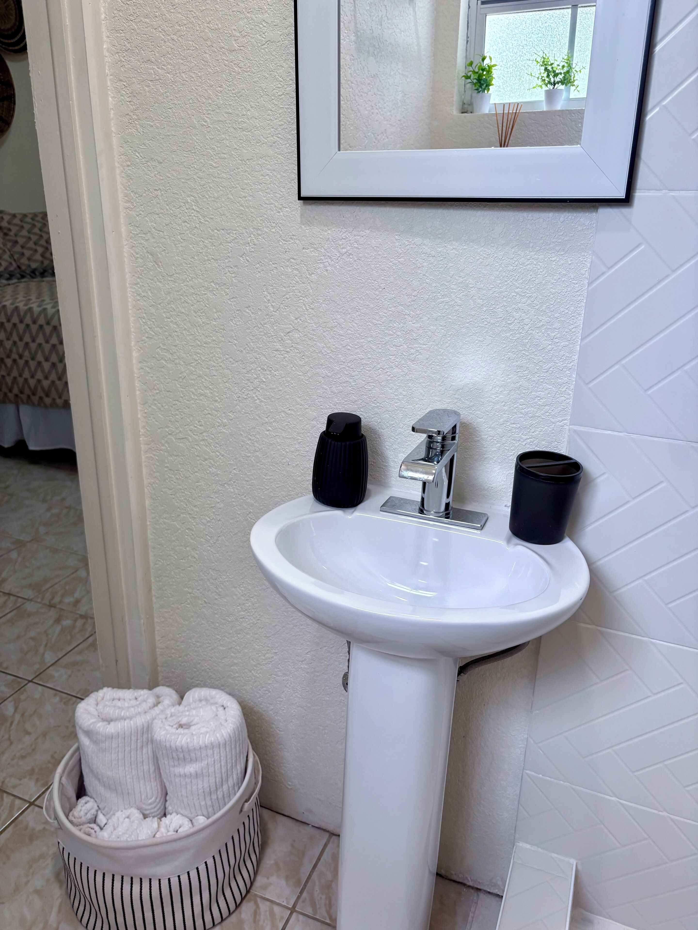 A bathroom with a white sink, two black soap dispensers, a mirror above the sink, and a towel basket with towels.