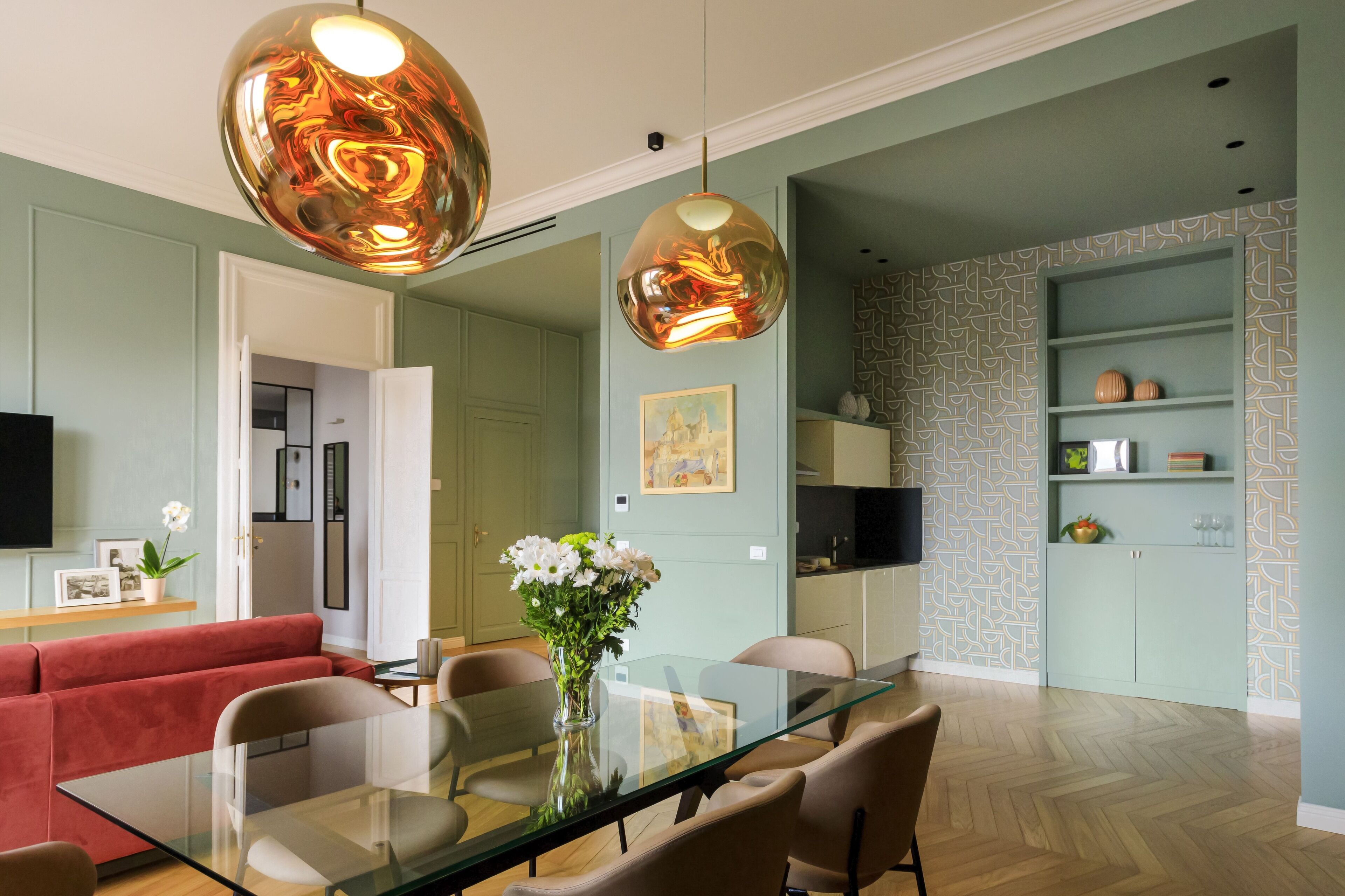 A modern dining area with a glass table, red sofa, and pendant lights.