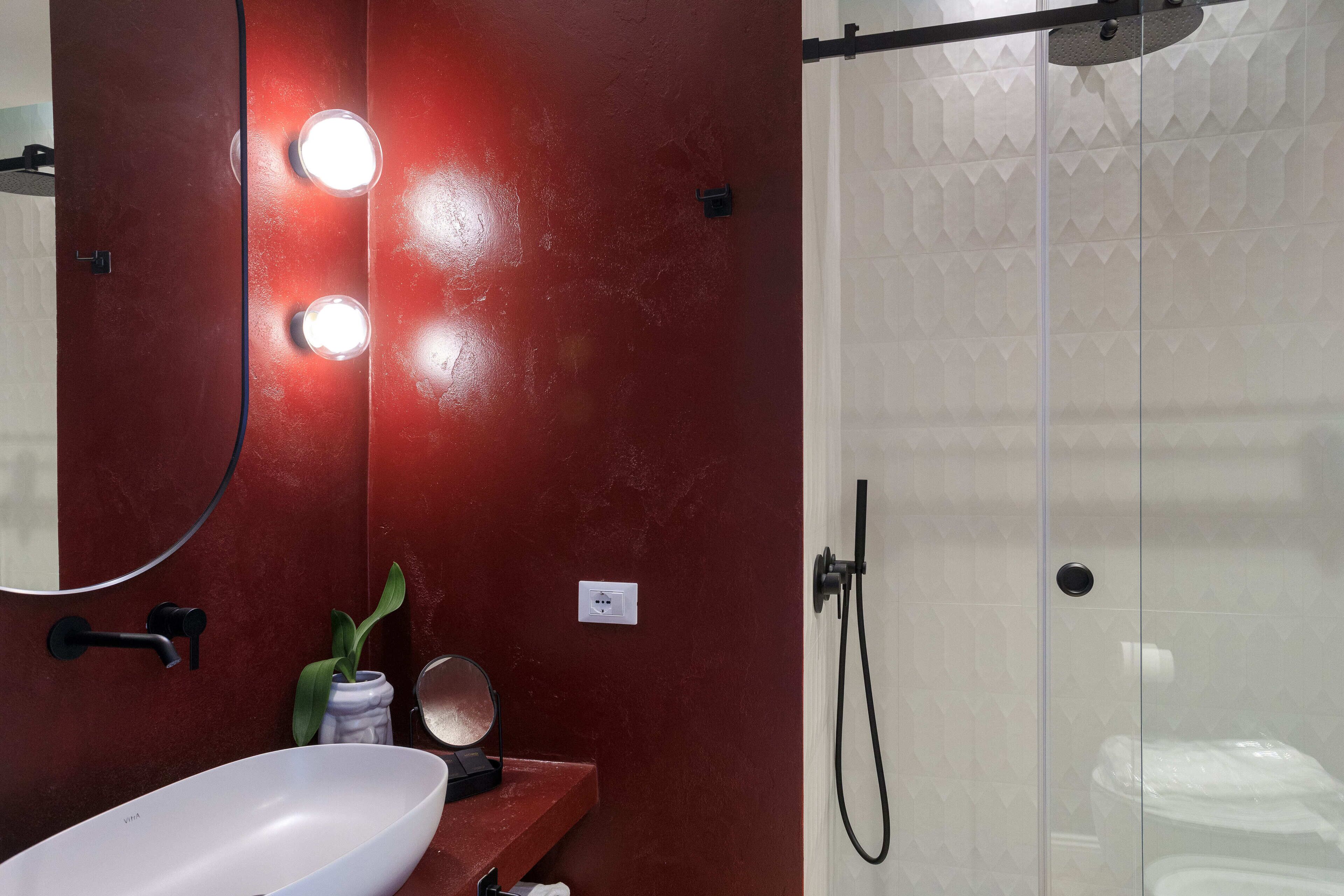 Casa de banho com toucador vermelho, lavatório branco, espelho e cabine de duche em vidro.