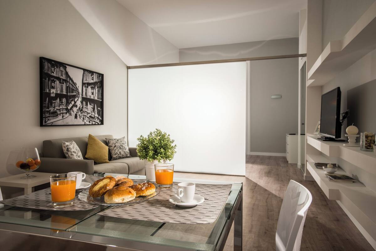 Un salon moderne avec une table à manger en verre, des aliments pour le petit-déjeuner, un canapé, une table basse et un téléviseur.