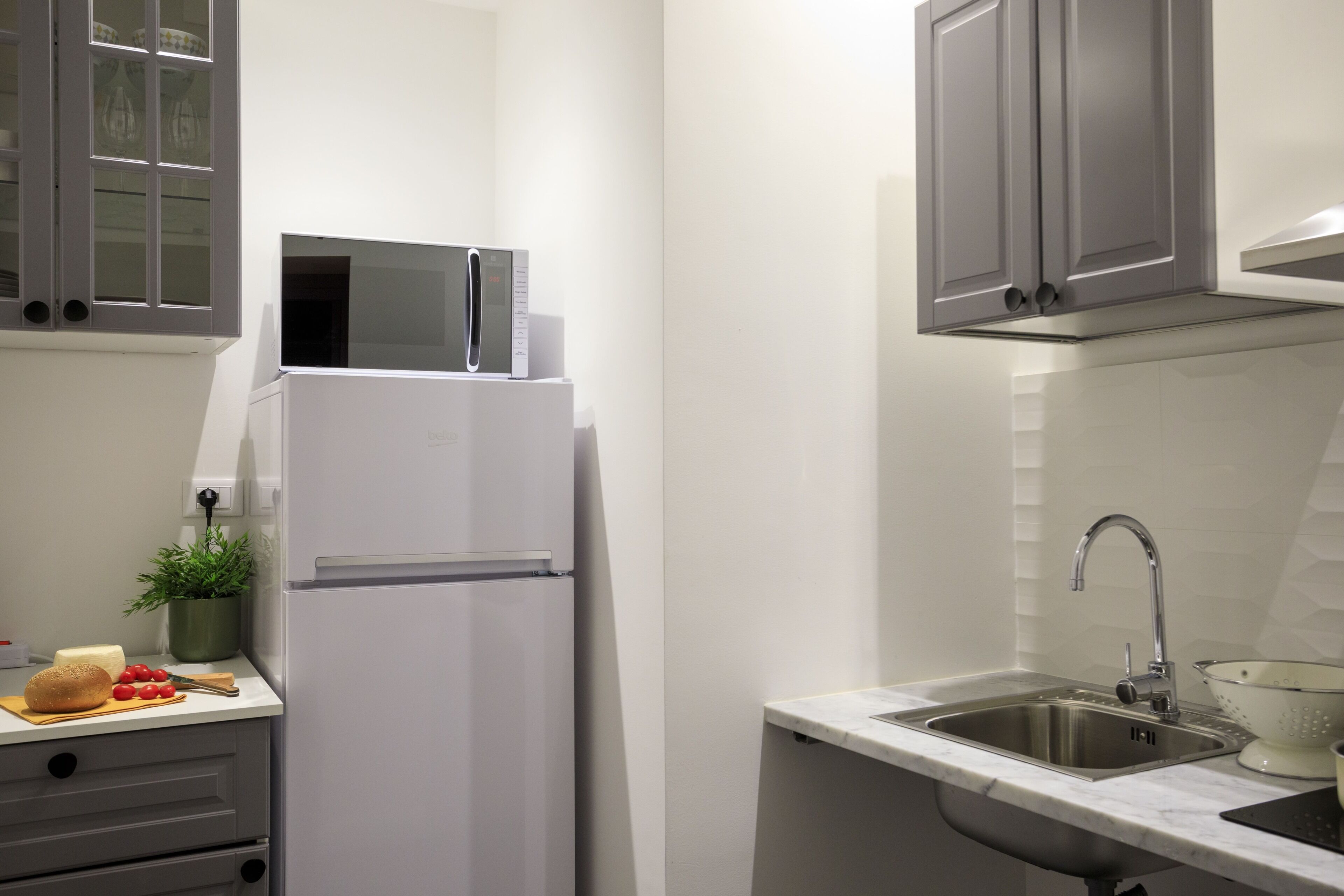 A compact kitchen with a white refrigerator, a sink, and grey cabinets.