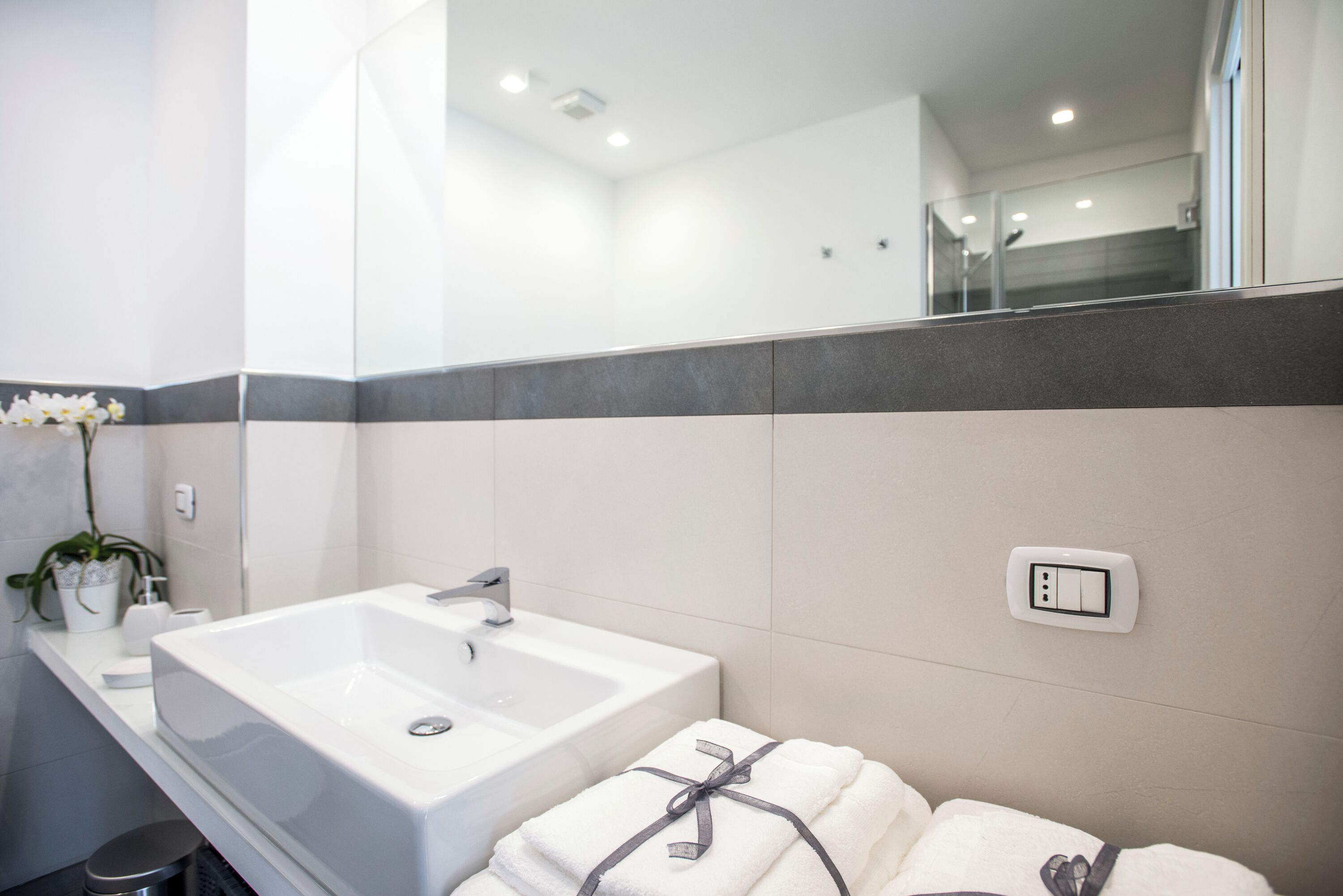 Ein modernes Badezimmer mit einem weißen Waschbecken, einem Spiegel und einem Handtuchhalter.