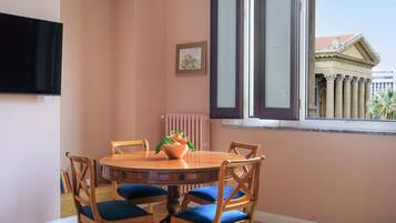 Un comedor con una mesa redonda de madera, sillas con cojines azules, un frutero y un cuadro en la pared.