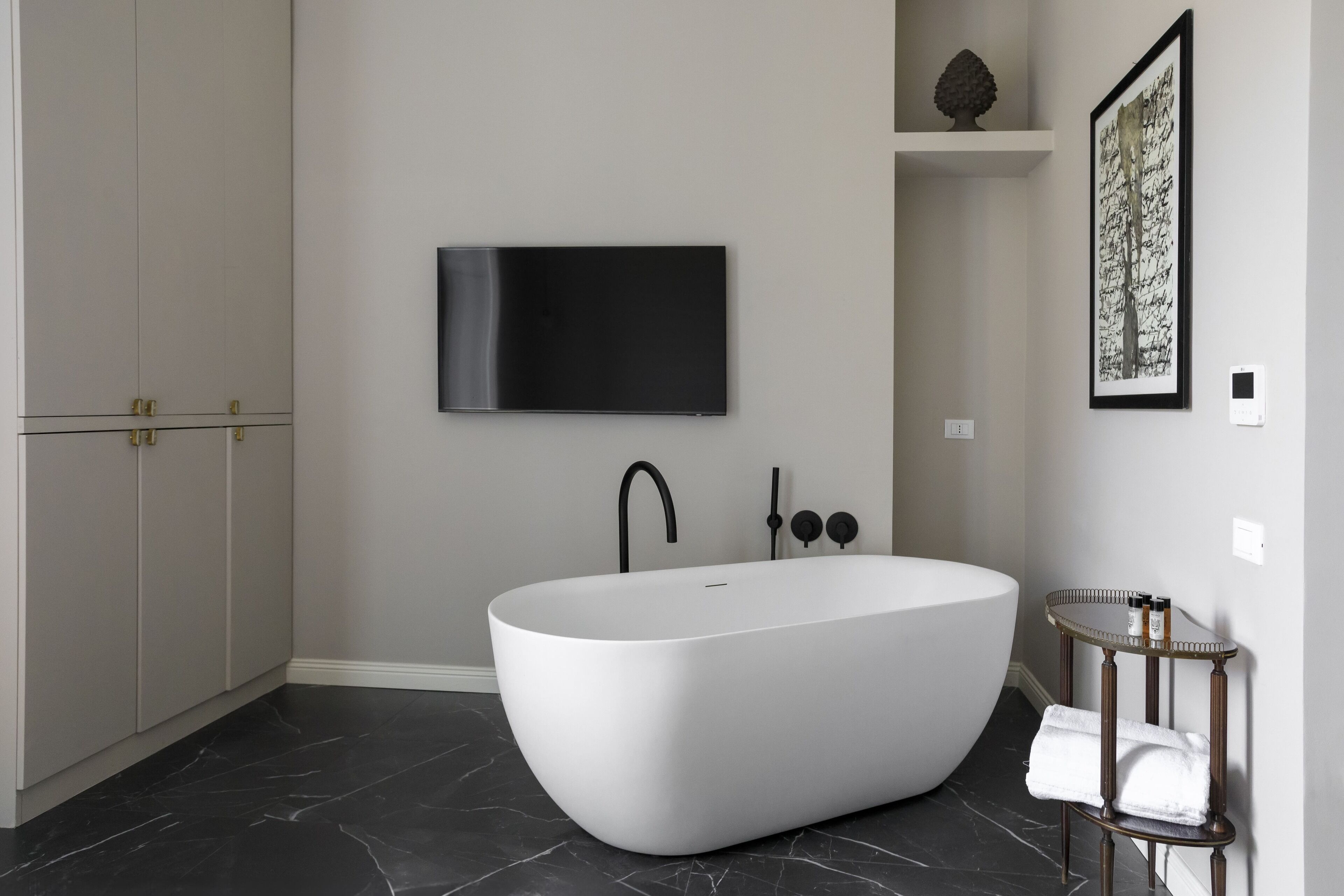A modern bathroom with a freestanding bathtub, a mounted TV, and a small table with toiletries.