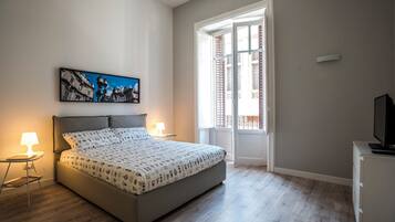 A bedroom with a bed, bedside lamps, a television, a window with shutters, and a framed picture on the wall.