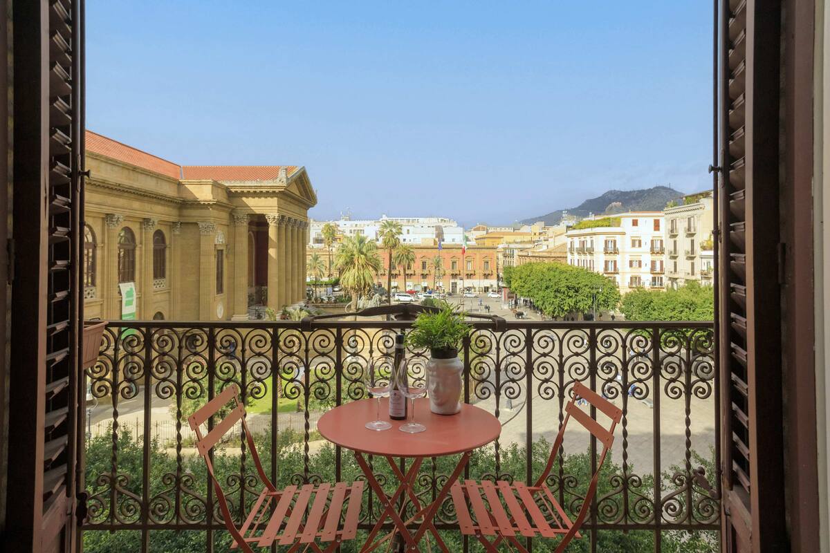 Un balcon avec une table et des chaises, d’où l’on peut admirer un panorama sur la ville, avec ses bâtiments et une montagne en arrière-plan.