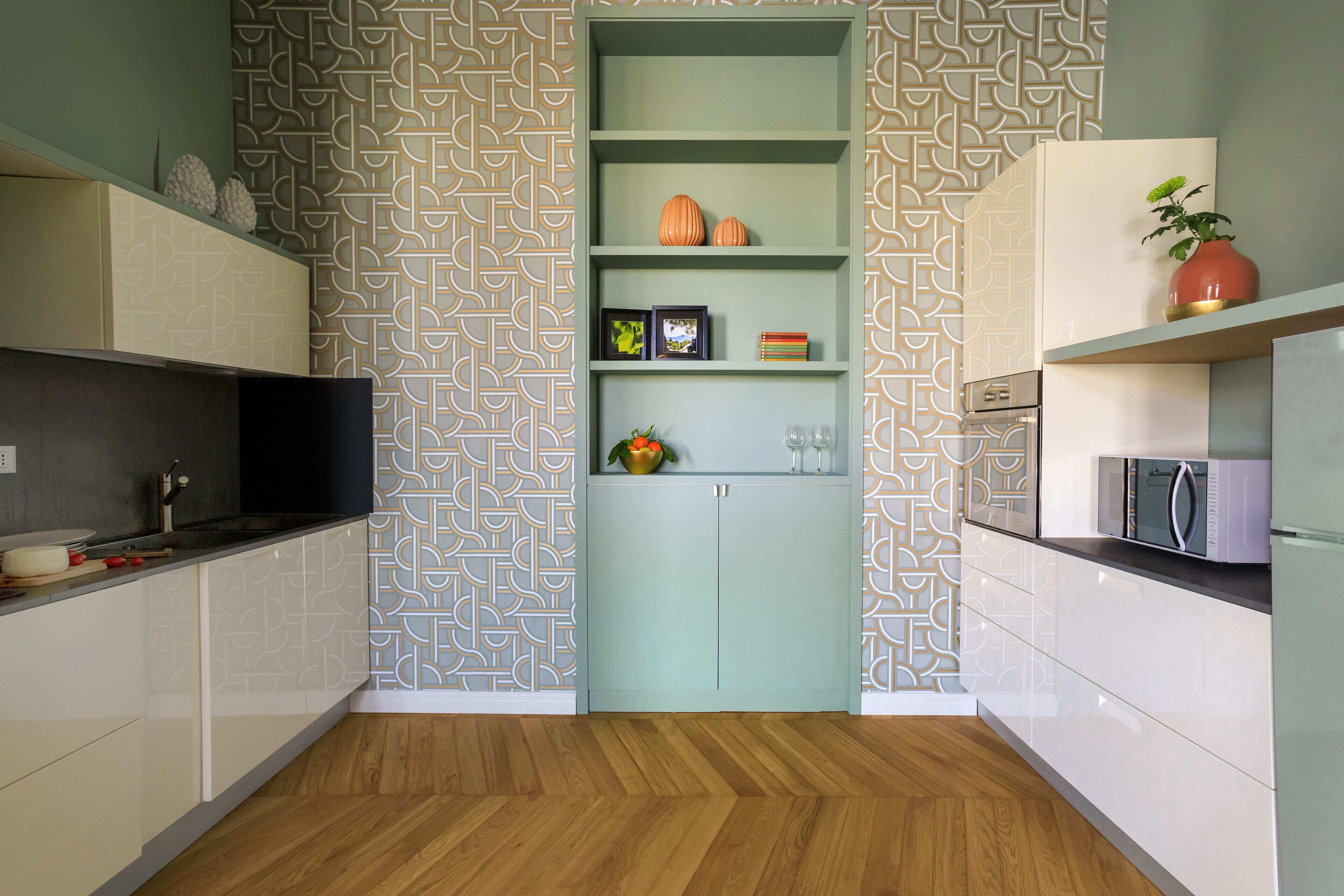 A modern kitchen with white cabinetry, a herringbone wood floor, and a geometric patterned wall.