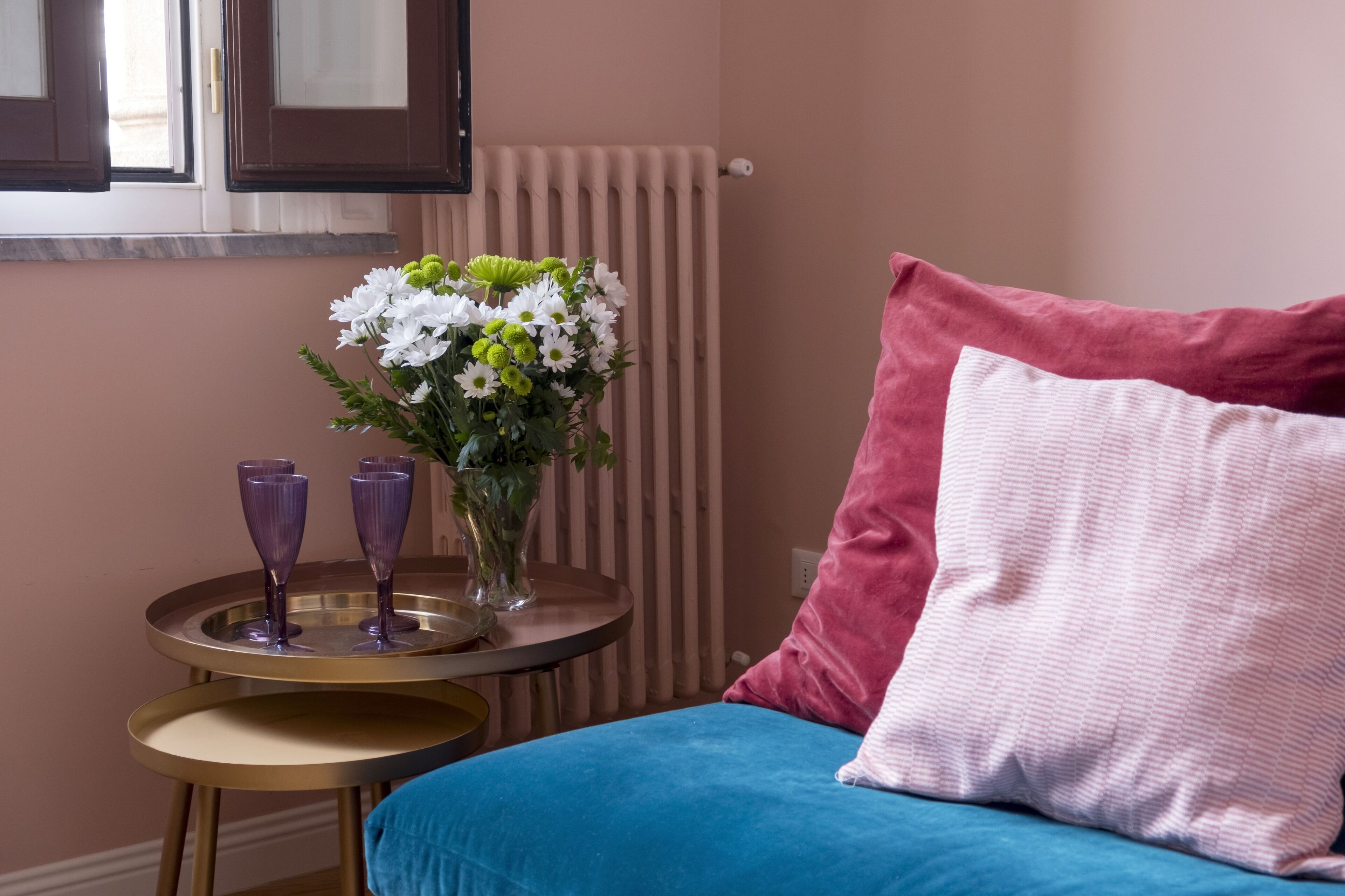 Una habitación con una cama, una mesa redonda con un florero y dos vasos morados.