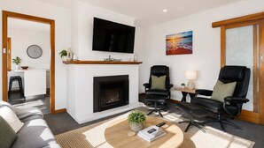 A modern living room with a fireplace, a flat-screen TV, two leather chairs, a sofa, and a coffee table with a book and remote controls. - Residential Retreat, Groups & Families-Sleeps 15 (Warrane)
