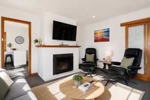 Una sala de estar moderna con chimenea, un televisor de pantalla plana, dos sillones de cuero, un sofá y una mesa de centro con un libro y controles remotos.