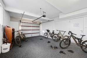 Un garaje con bicicletas, una puerta de madera y un cubo blanco.
