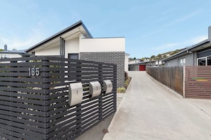 A modern residential building with a gated driveway, numbered mailboxes, and a clear sky.