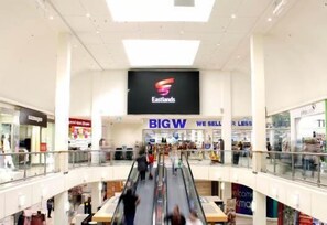 A multi-level shopping mall with an escalator in the center, surrounded by various stores including a prominent EASTLANDS sign.
