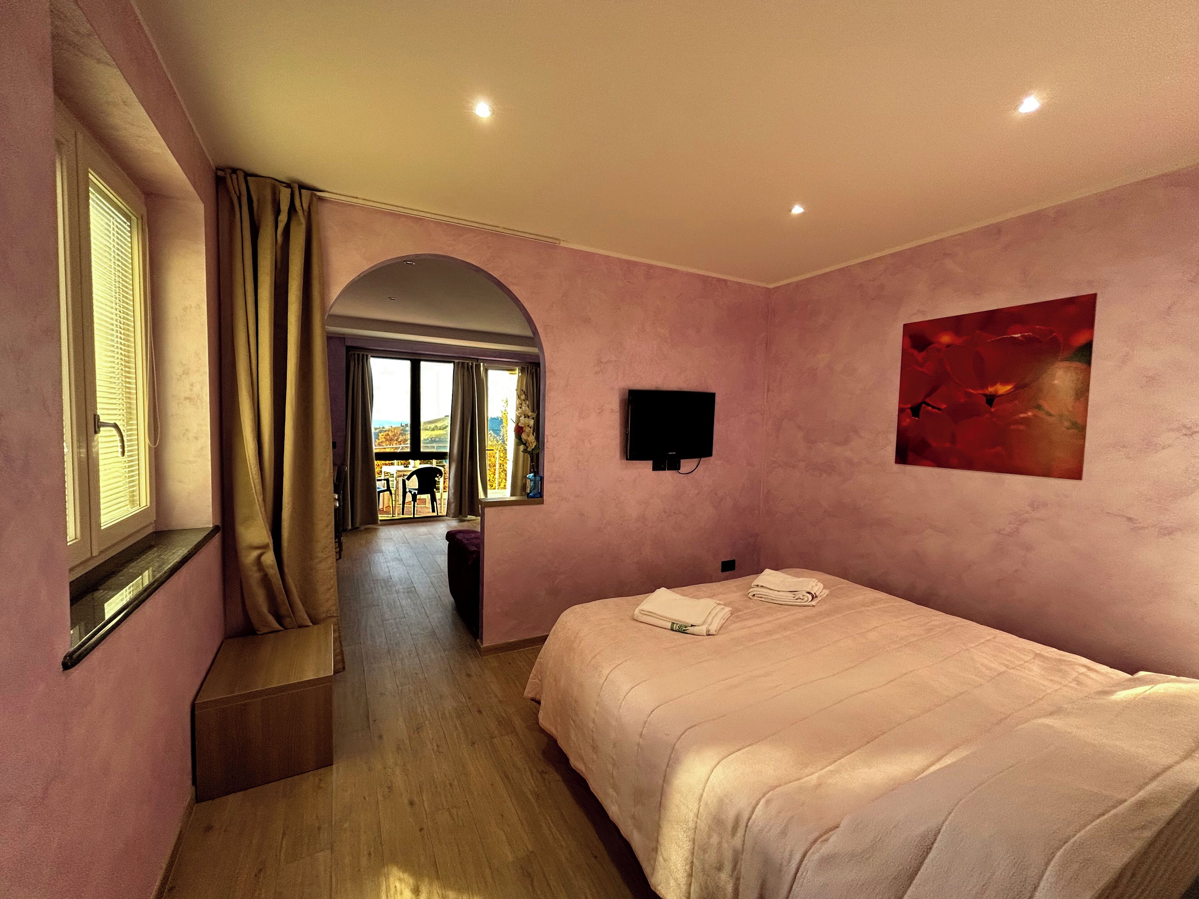 A bedroom with a bed, a TV, a painting, and a window with curtains.