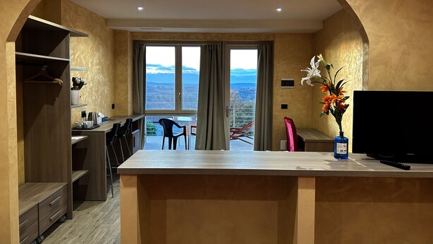 A modern kitchen with a large island, a dining area with chairs, a TV, and a view of the mountains through the windows.
