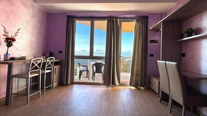 A modern room with a wooden floor, a dining area with chairs, a table, and a view through a large window.