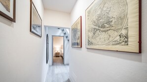 A hallway with framed artworks on the walls, a staircase leading to another room, and a bed with a nightstand in the distance. - YiD Donatello con terrazzo (Florence)
