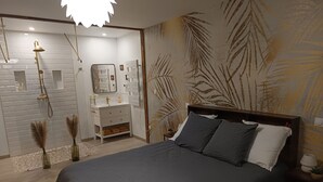 A modern bedroom with a large bed, a vanity with a mirror, and a shower area. - Maison D'hôtes L'atelier Détente et Spa Animaux Acceptés Jacuzzi, Sauna = Option (Caudrot)