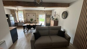 A cozy living room with a sofa and a dining area with a table and chairs. A kitchen is visible in the background with a refrigerator and a microwave. - Maison D'hôtes L'atelier Détente et Spa Animaux Acceptés Jacuzzi, Sauna = Option (Caudrot)