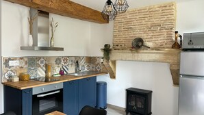 A kitchen with a rustic brick wall, a wooden ceiling, and a modern stove. - Maison D'hôtes L'atelier Détente et Spa Animaux Acceptés Jacuzzi, Sauna = Option (Caudrot)