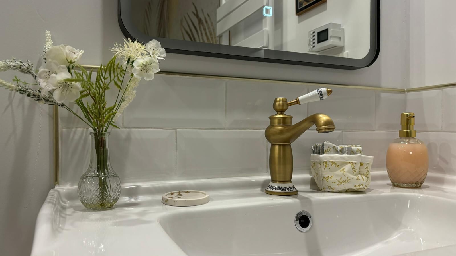 A bathroom sink with a gold faucet, a vase of white flowers, and two toiletry bottles.