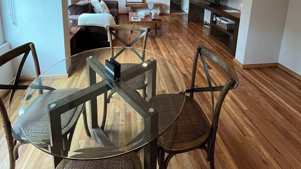 Una sala de estar moderna con una mesa de comedor de vidrio, sillas de madera, un sofá y un televisor.