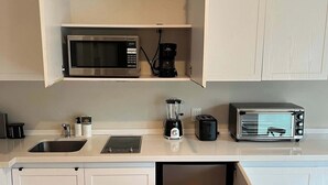 Una cocina compacta con muebles blancos, microondas, cafetera, tostadora y lavavajillas.