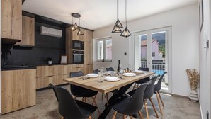 A modern kitchen with wooden cabinets, a black countertop, and a dining area with a wooden table and black chairs. - Pool House Beba Tribalj Lake (Vinodol)