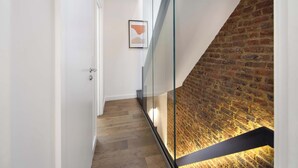 A modern interior with a glass railing, a brick wall, and a wooden floor. - 1 Min Walk to Euston Station | Luxury Townhouse (London)