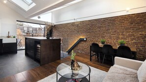 A modern loft with a kitchen, dining area, and living space, featuring a brick wall, skylights, and a staircase. - 1 Min Walk to Euston Station | Luxury Townhouse (London)