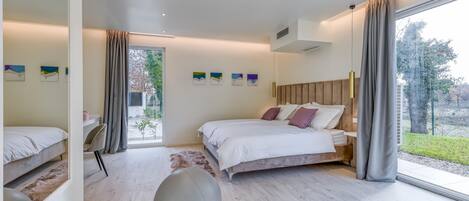 A modern bedroom with a large bed, a desk, and a view of the outdoors.