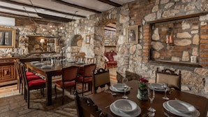 A stone-walled dining area with a wooden table set for four, red upholstered chairs, and a stone fireplace. - Pool Villa Cupido in Crikvenica - Drivenik (Vinodol)