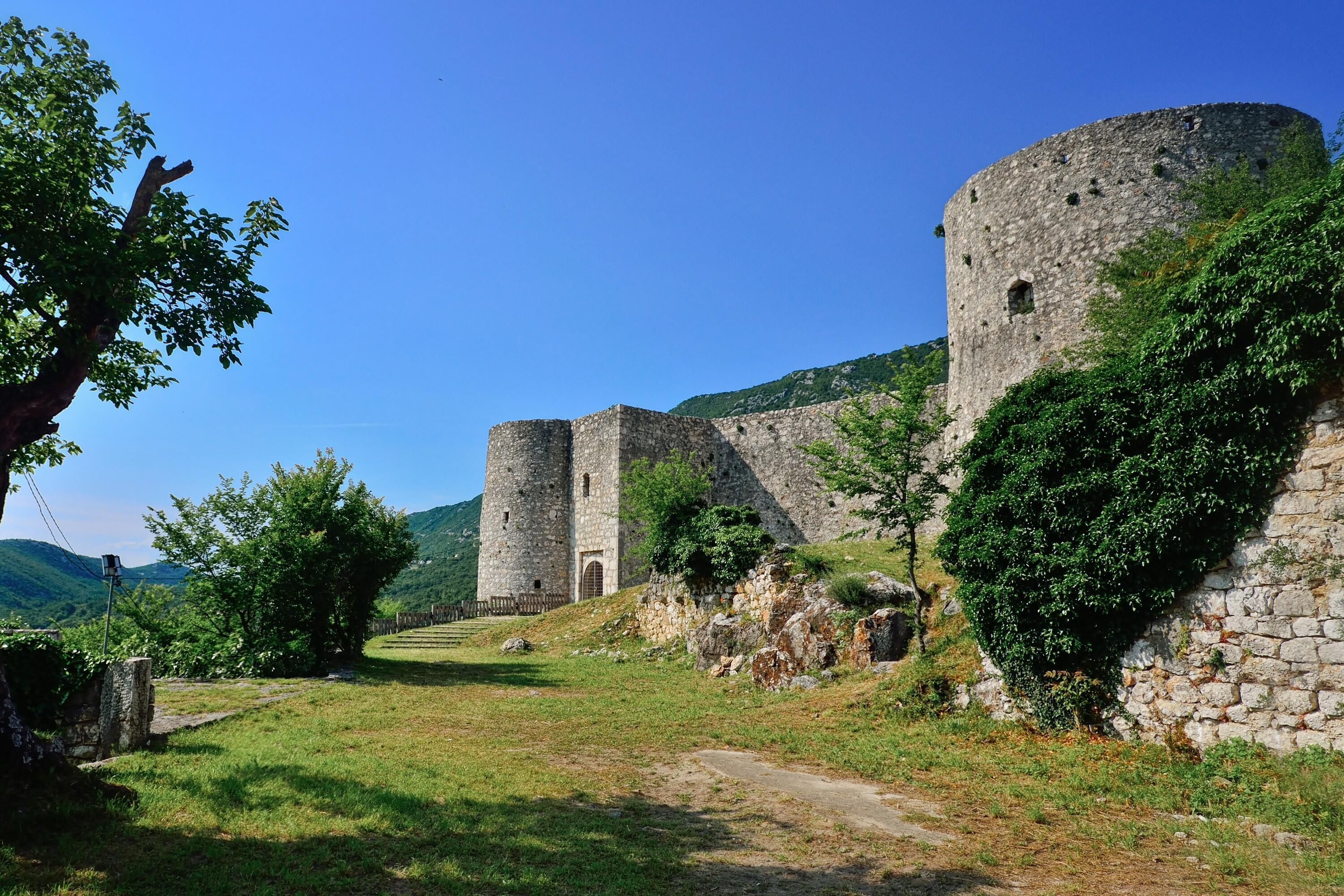 A historic stone castle with a central tower and a surrounding wall, set in a lush green landscape.