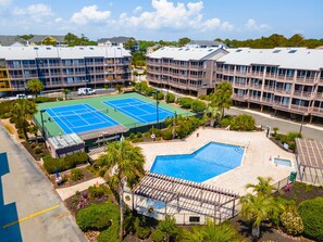 A hotel with multiple floors, a tennis court, and a swimming pool.