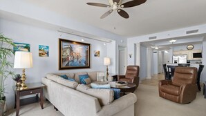 A living room with a sofa, coffee table, and two chairs. There is a painting on the wall, a lamp, and a ceiling fan. - Waves and Relaxation: 2Bdrm Condo with Jetted Tub (North Myrtle Beach)