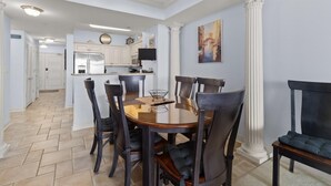 A dining area with a round table and chairs, a kitchen in the background, and a large column. - Waves and Relaxation: 2Bdrm Condo with Jetted Tub (North Myrtle Beach)
