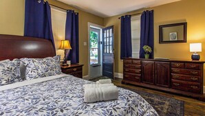Une chambre à coucher avec un grand lit, une commode, une table de chevet, une lampe et une porte donnant sur l’extérieur.