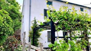 A white building with a black wooden structure in front, surrounded by greenery. - House Viskic (Rab)