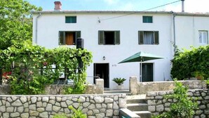 A two-story building with a stone wall in front, a green umbrella, and a small potted plant. - House Viskic (Rab)