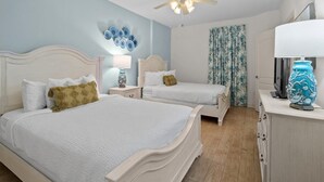 A bedroom with two beds, a ceiling fan, a decorative wall, a nightstand, a lamp, and a television. - Beachfront Escape: Oceanview 2 Bedroom Condo (North Myrtle Beach)