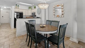 A dining area with a round table, six chairs, and a chandelier. - Beachfront Escape: Oceanview 2 Bedroom Condo (North Myrtle Beach)