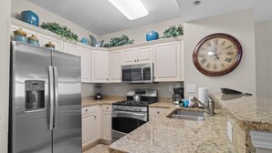 A modern kitchen with stainless steel appliances, a granite countertop, and a wall-mounted clock.